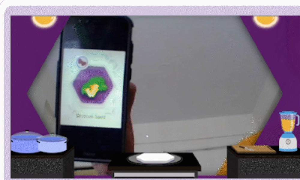 The augmented reality screen, a phone held over a card showing a broccoli seed in the game kitchen.